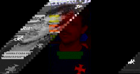 Homem com camiseta preta e fundo de banners esportivos.