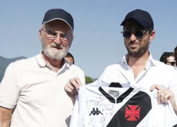 Homens segurando camisa do Vasco com assinatura e escudo.