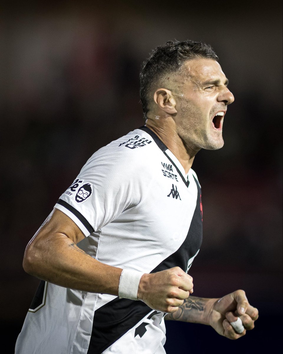 20251027-084050-1-1-1-1 Imagem de jogador de futebol masculino em ação celebrando com expressão de emoção, vestido com uniforme branco com detalhes pretos, cabelo curto e rotina de esforço físico em campo.