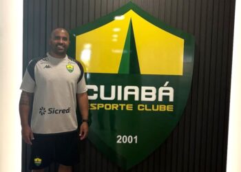 Cinegrafista com uniforme do Vasco ao lado do escudo do clube.