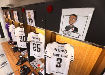 Jogadores do Vasco em frente ao armário com uniformes e caricaturas.