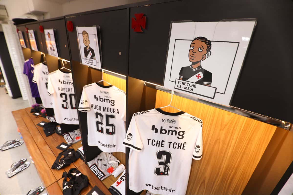 Jogadores do Vasco em frente ao armário com uniformes e caricaturas.