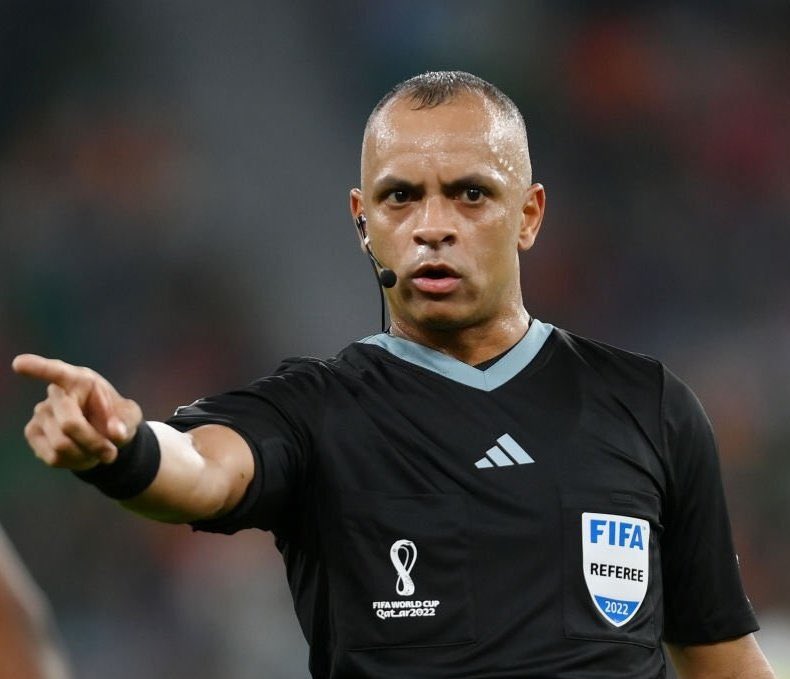 20251030-162850-1-1-1-1 Árbitro de futebol apontando, uniforme preto com distintivo FIFA.