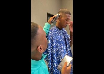 Jovem sendo atendido na barbearia com máquina de corte.