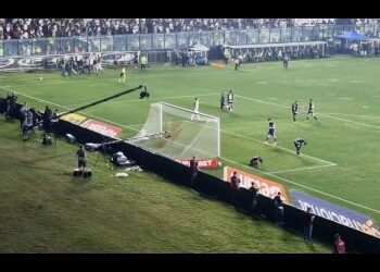Jogadores em campo durante partida de futebol no estádio.