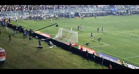 Jogadores em campo durante partida de futebol no estádio.