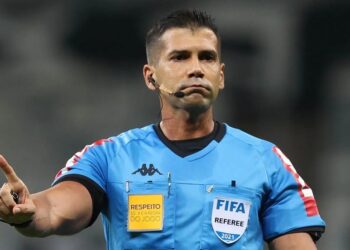 Árbitro de futebol com uniforme azul e microfone.