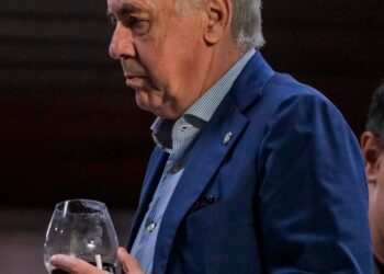 Homem idoso segurando taça de vinho.