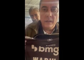 Homem falando ao celular com fundo de pessoas.