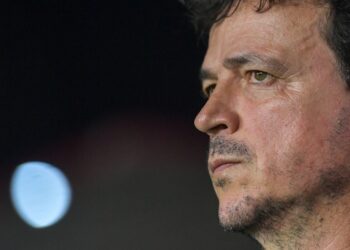 Fotografia de um homem observando atentamente, com expressão séria e focada, com fundo escuro.