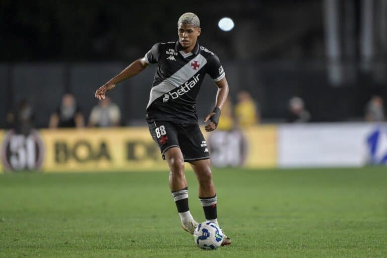 Jogador do Vasco em campo com bola nos pés, durante jogo noturno.