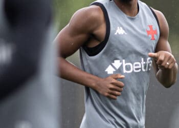 Futebolista treinando sob chuva com uniforme cinza do Vasco.