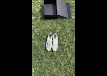 Tênis branco com detalhes azuis sobre grama verde.