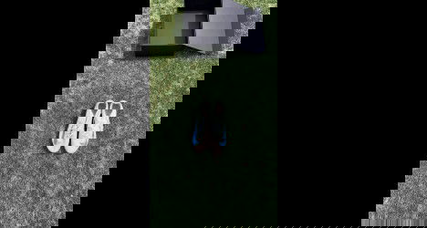 Tênis branco com detalhes azuis sobre grama verde.