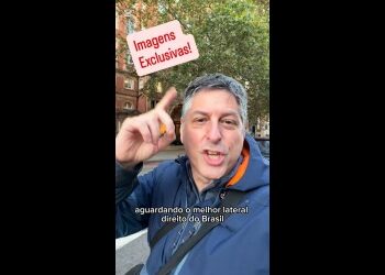 Homem apontando para cima, em rua com árvores ao fundo.