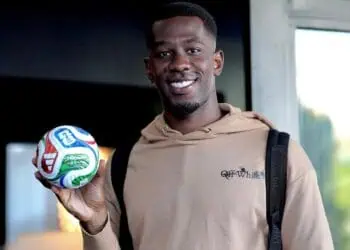 Jogador segurando bola de futebol com sorriso.