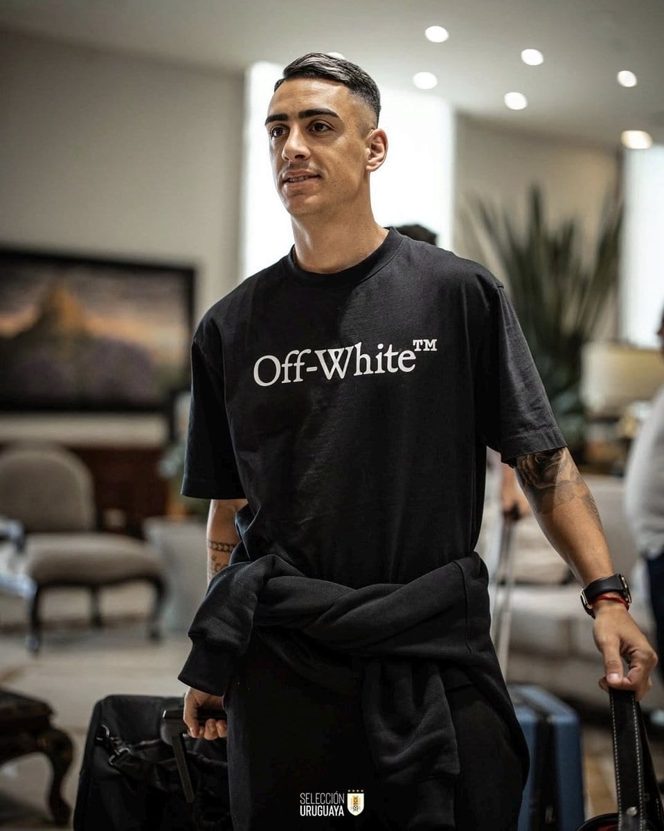 Vasco em aeroporto, homem com mala e roupa preta.