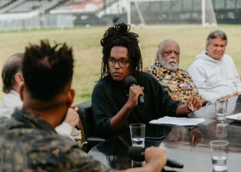 Mulher negra fala em reunião ao ar livre com microfone.