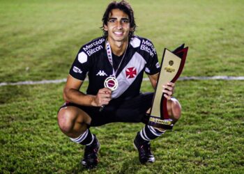 Goleiro com medalha e troféu no gramado.