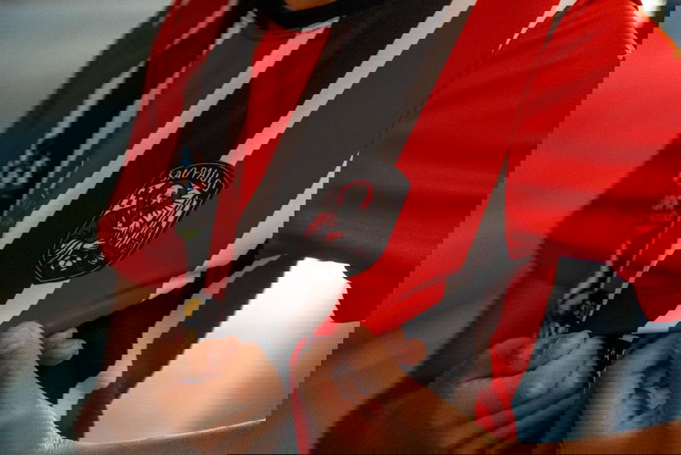 São Paulo Futebol Clube camiseta, detalhe do escudo, jogador segurando a camisa vermelha e preta.