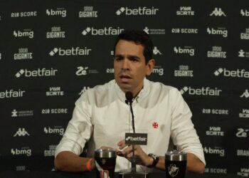 Jorge Salgado em coletiva de imprensa vestindo camisa branca com escudo do Vasco.