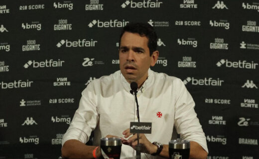 Jorge Salgado em coletiva de imprensa vestindo camisa branca com escudo do Vasco.
