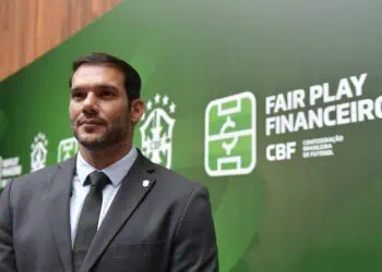 Imagem de homem de terno na frente de painel verde com logos do CBF e da Confederação Brasileira de Futebol, promovendo jogo limpo e finanças transparentes.