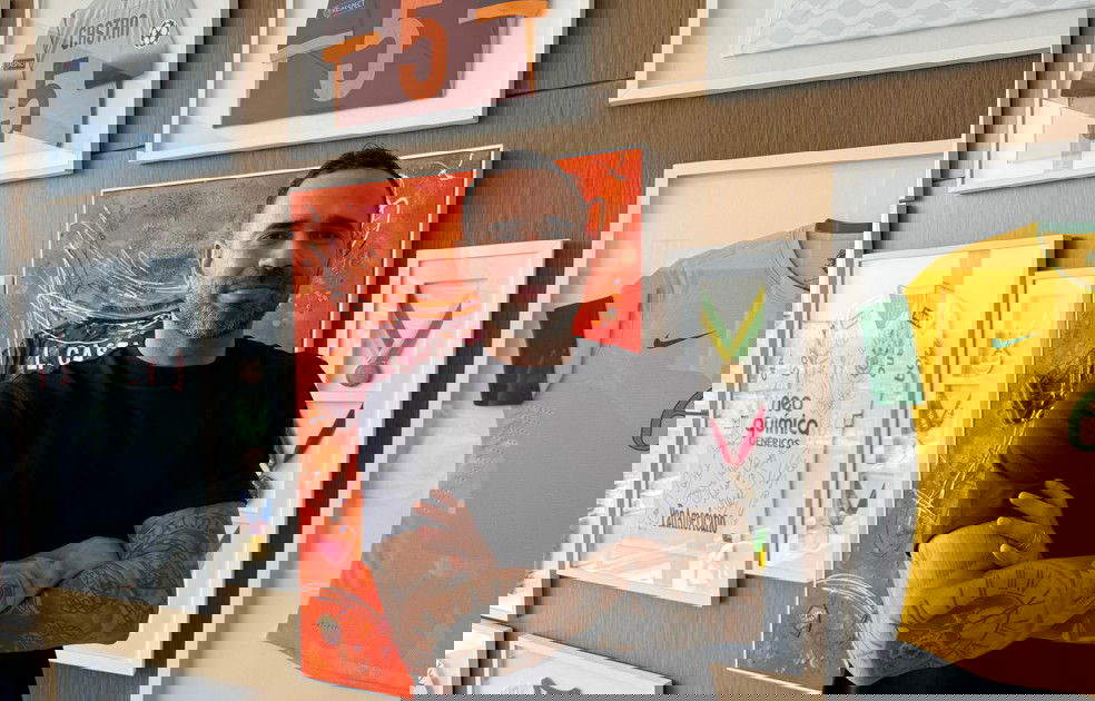 Vestido preto com braços cruzados em exibição de troféus e camisas de futebol.