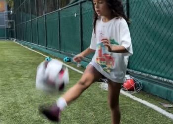 Bebê chutando bola de futebol no gramado.