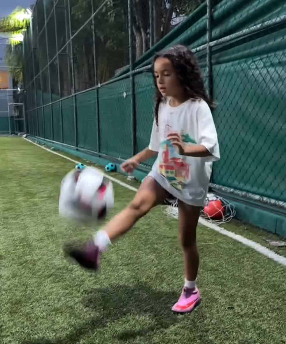Bebê chutando bola de futebol no gramado.