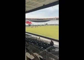 Campo do estádio com arquibancadas vazias e céu claro ao fundo.