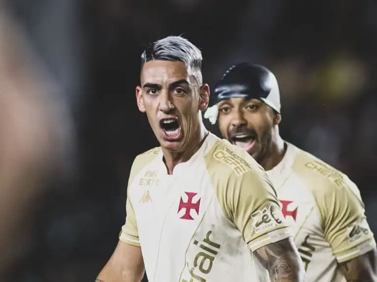 Jogador comemorando gol com torcida ao fundo.