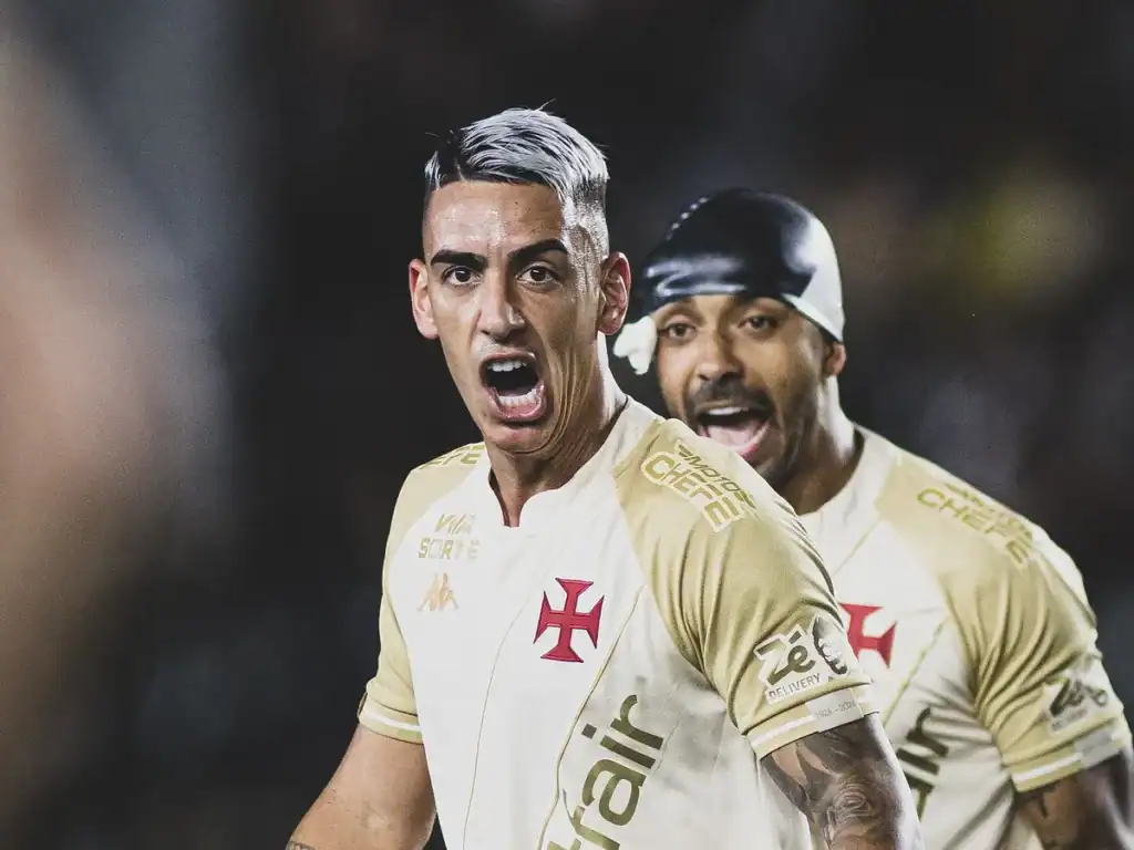 Jogador comemorando gol com torcida ao fundo.