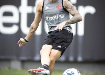 Jogador de futebol treinando com a bola no campo, vestindo uniforme cinza e preto.