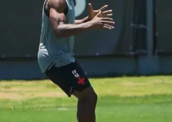 Atleta treinando com cones em campo de futebol.