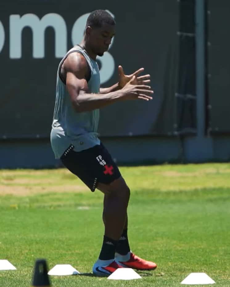 Atleta treinando com cones em campo de futebol.
