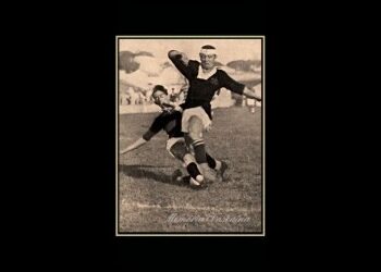 Jogador de futebol em ação com a bola no campo.