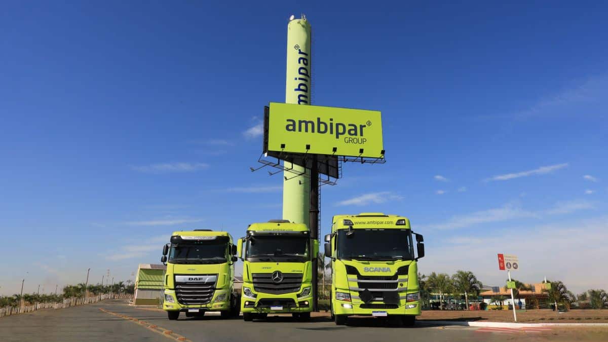 Três caminhões verdes estacionados sob poste publicitário.