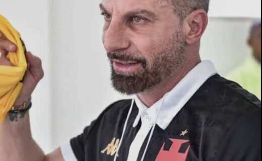 Homem com camiseta do Vasco, segurando roupa amarela.