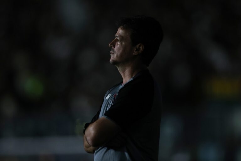 2. Homem de perfil pensativo, braços cruzados, fundo escuro, vestindo uniforme de treino do Vasco com detalhes em preto e branco.