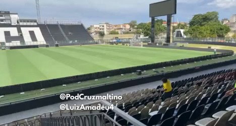 Vista do campo de futebol do estádio Vasco, com assentos e gramado bem cuidado, sob céu claro.