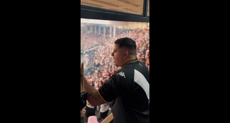 Homem vestindo camisa do Vasco comemora ao assistir jogo em estádio cheio.