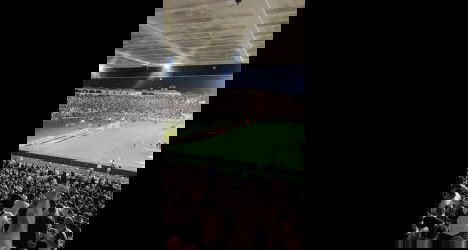 Vista aérea do estádio lotado, torcida vibrando, campo em destaque, ambiente animado e energia de um jogo emocionante do Vasco.