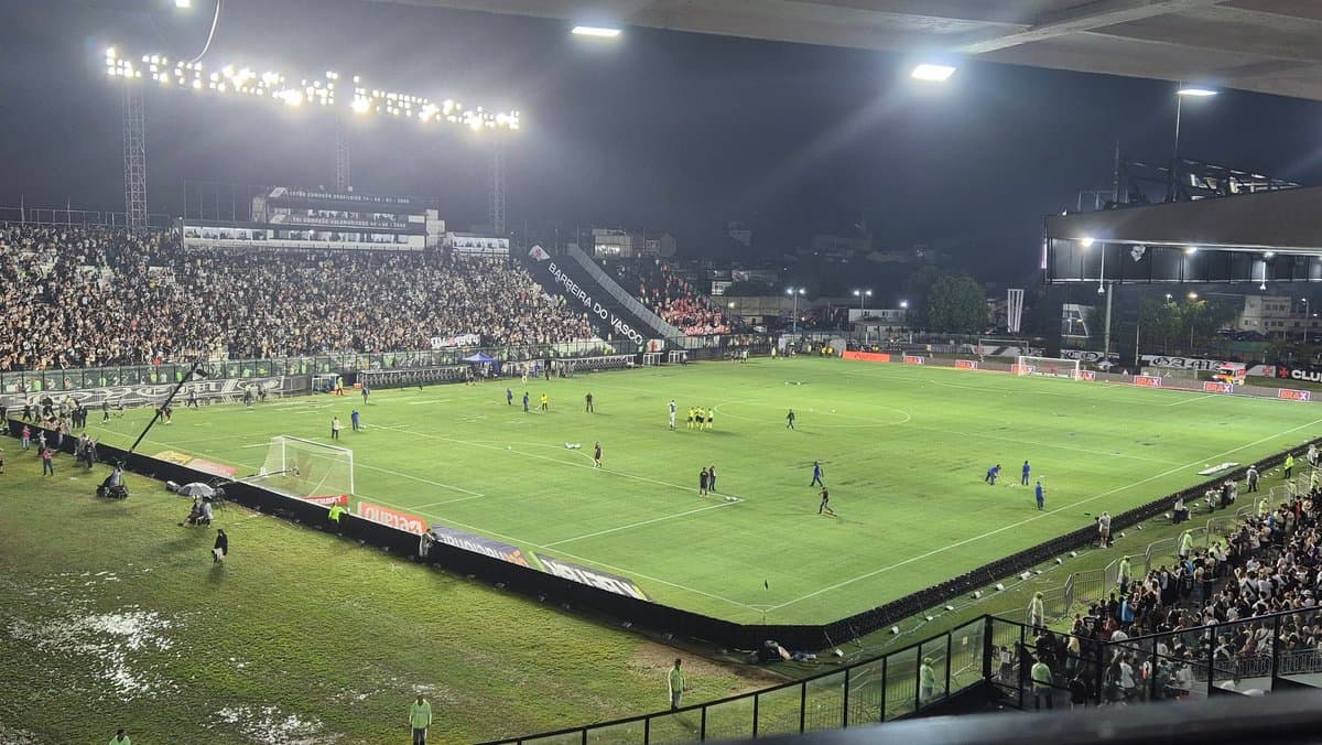 Estádio com torcedores, jogadores e iluminação potente.
