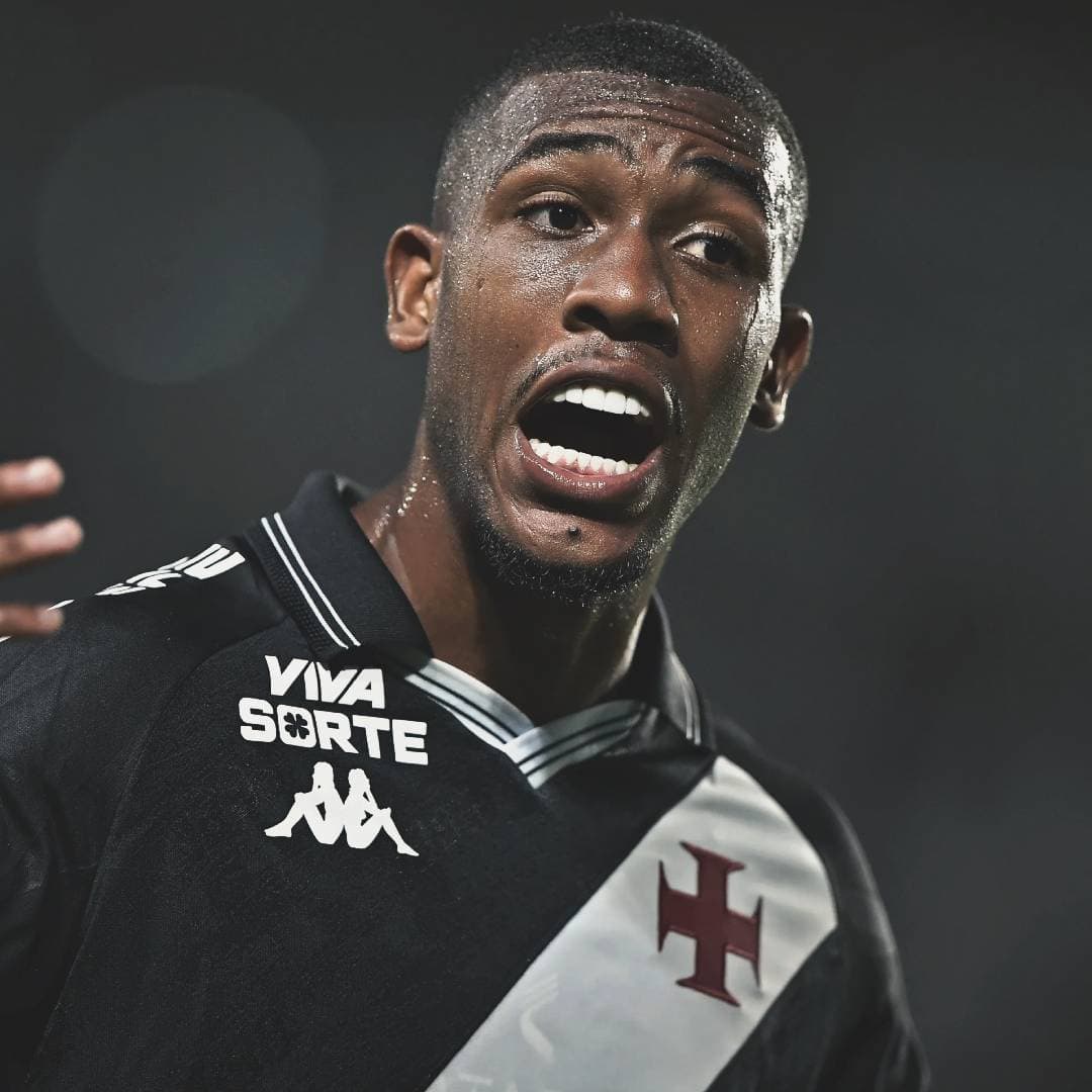 Jogador de futebol com uniforme preto e branco, rosto suado e expressão de esforço.