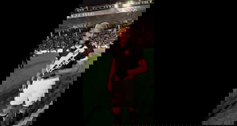 Jovem jogador do Vasco no estádio, sorrindo com uniforme preto e branco.