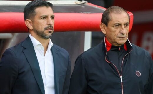 Homem de terno e homem de casaco preto em evento esportivo.