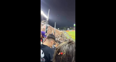 Torcedores do Vasco assistindo ao jogo no estádio, com iluminação de estádio ao fundo e clima de emoção e festa.