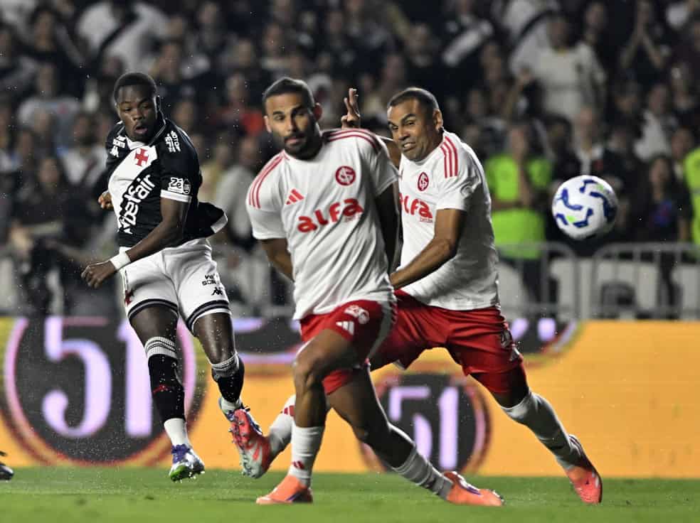 2. Alt: Jogadores do Vasco em ação durante jogo, com uniforme branco e vermelho, na torcida.
