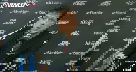 Alt: Pessoa falando em coletiva de imprensa do Vasco, com fundo de patrocinadores e logotipo do clube.